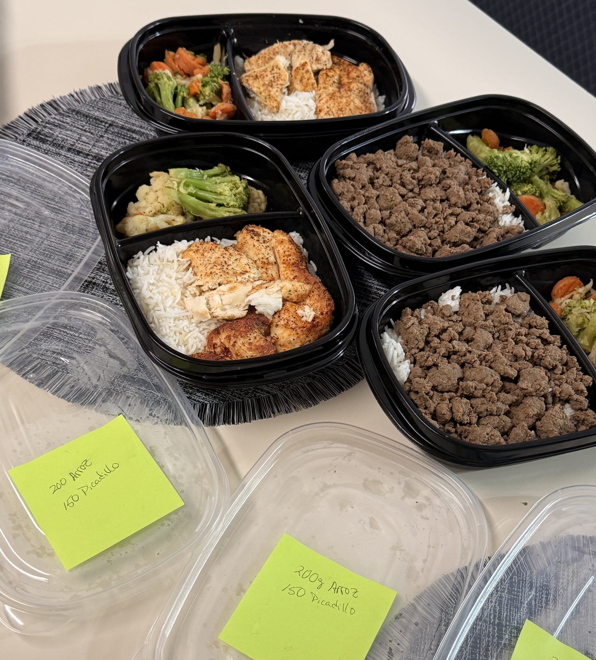 Cuatro envases de comida ya armados, con etiquetas escritas a mano que dicen 200 g de arroz y 150 de picadillo