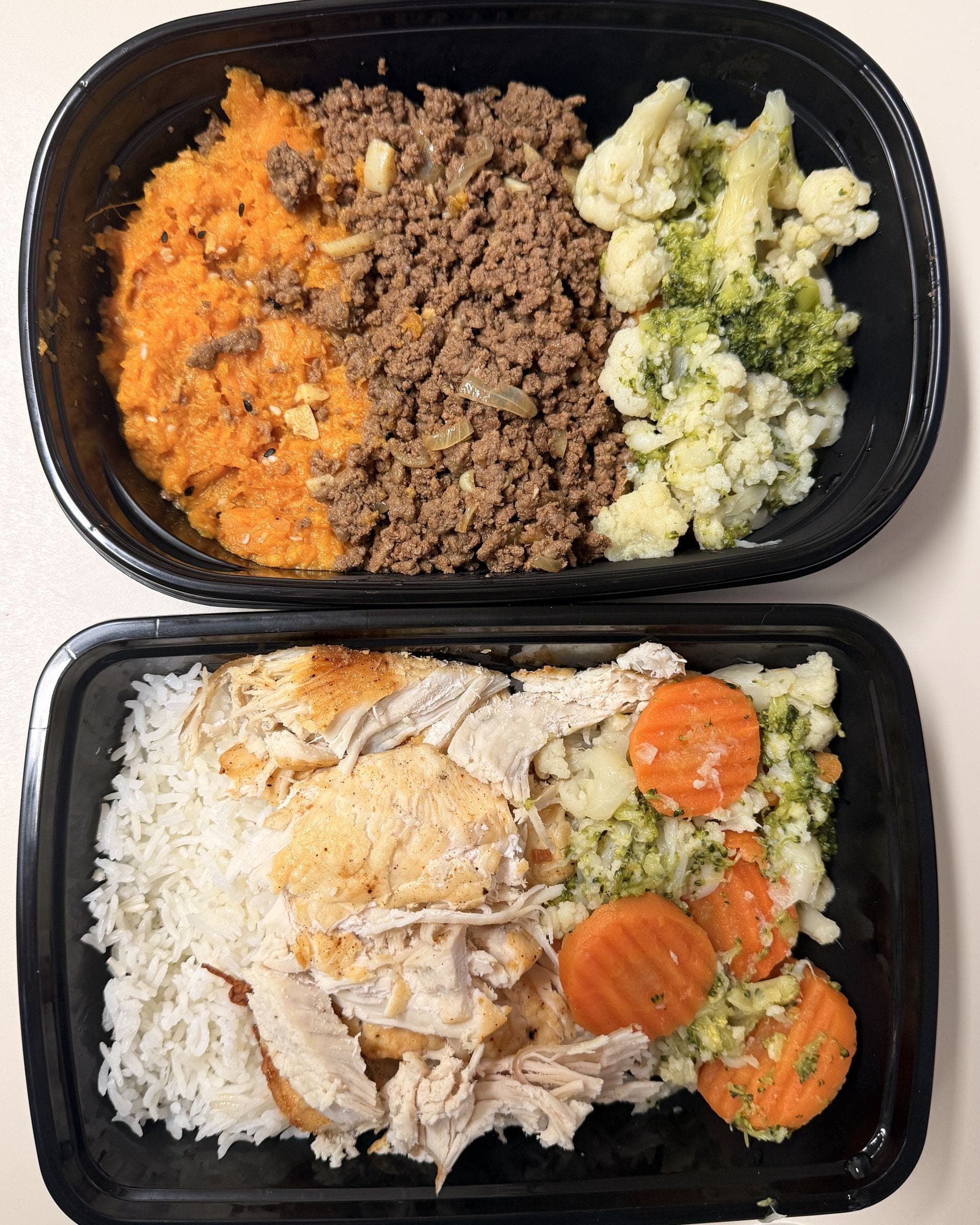 Dos envases de una jornada de producción, vistos desde arriba: picadillo de res con puré de camote, brócoli y coliflor, y pollo con arroz blanco y vegetales al vapor