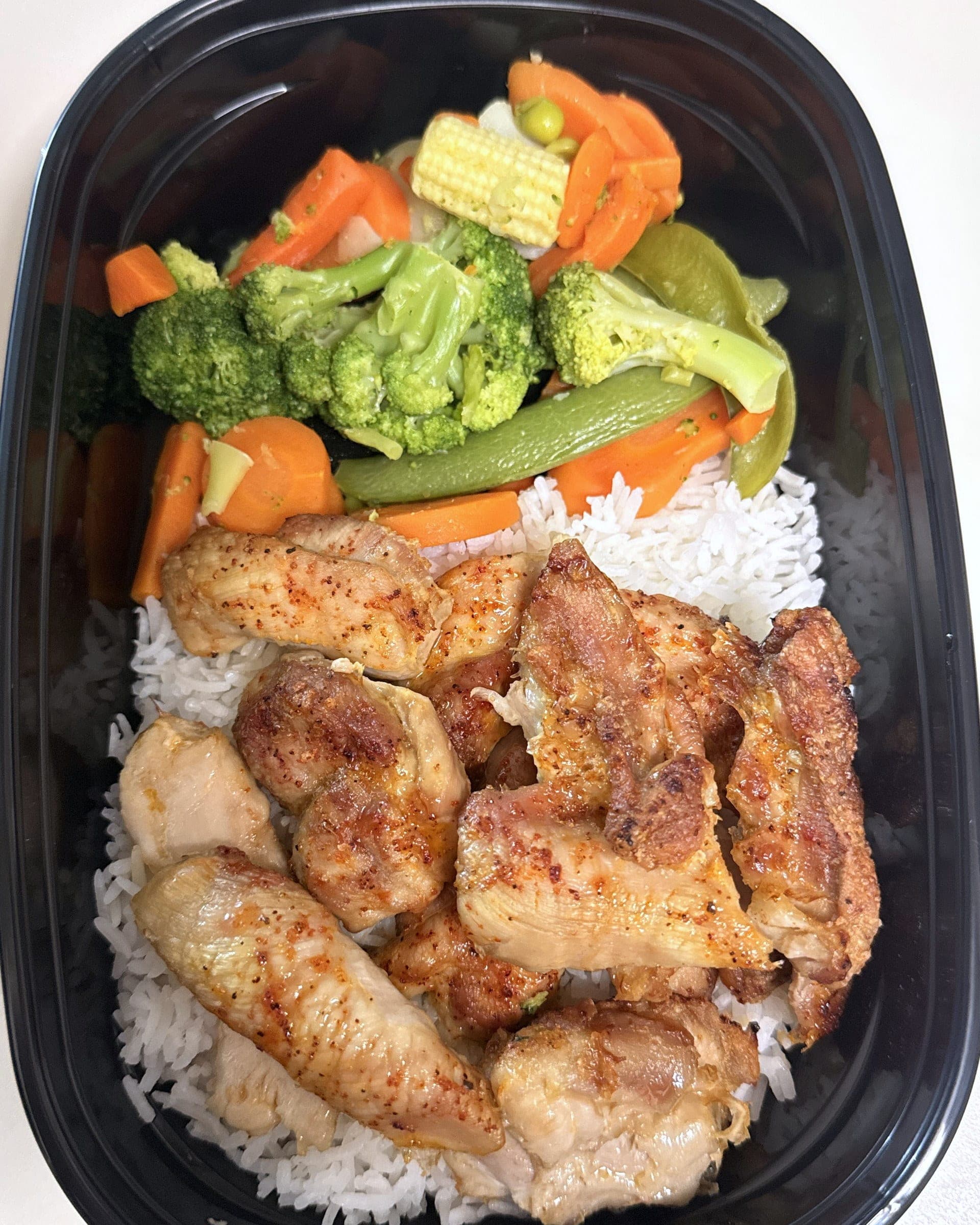 Trozos de pollo dorado sobre arroz blanco con vegetales al vapor