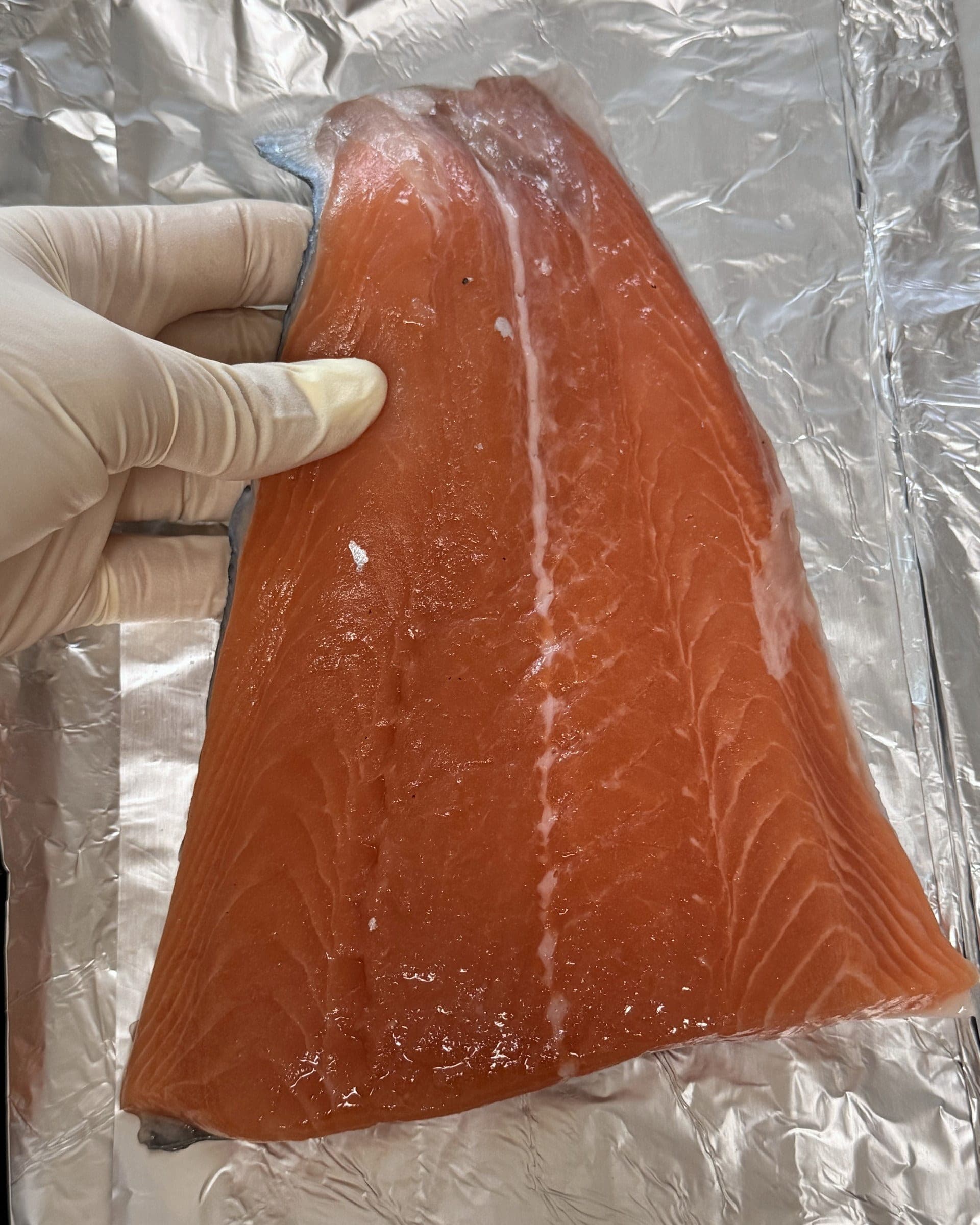 Mano sosteniendo un filete de salmón crudo sobre la bandeja del horno